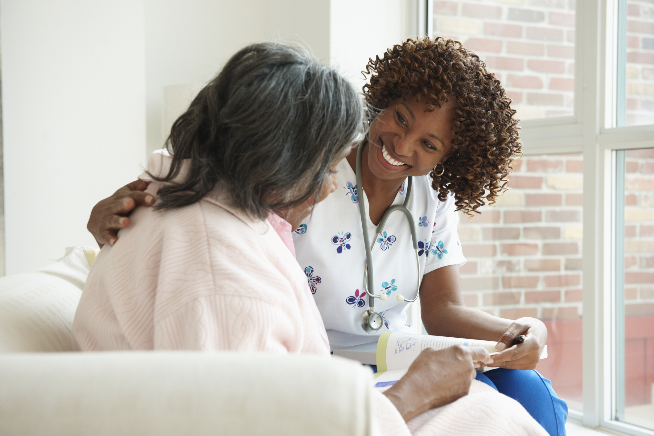 Smiling Nurse Looking At Book With Senior Patient