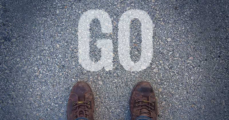 Closeup of feet on pavement with the word GO written on pavement