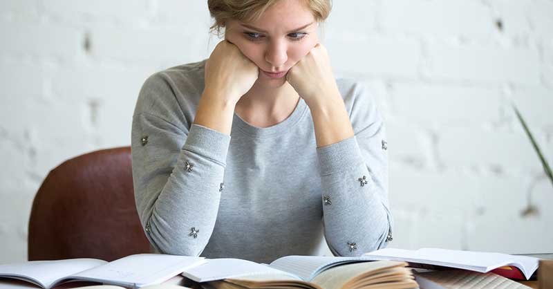 Woman sitting at desk bored whiled staring at lots of books